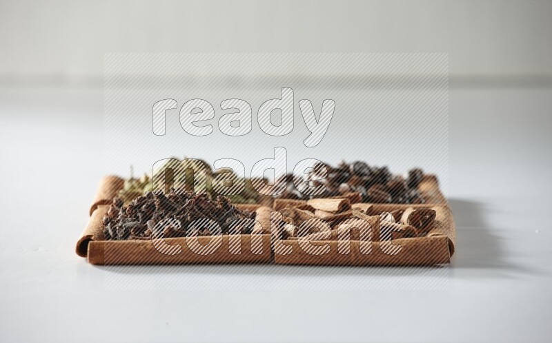 4 مربعات من أعواد القرفة ممتلئة بحبوب القهوة والقرفة والقرنفل والهيل على أرضية بيضاء