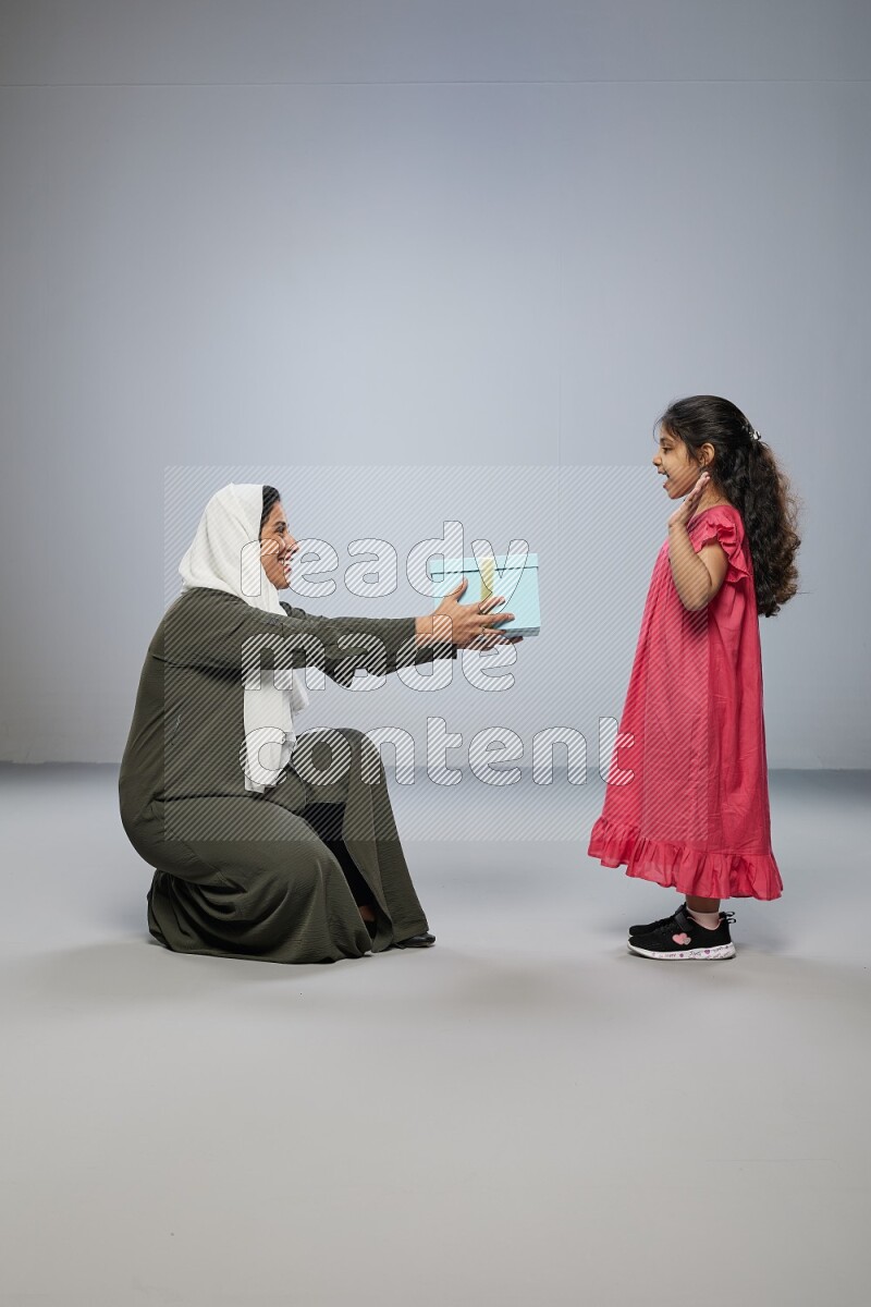 A girl giving a gift to her mother on gray background