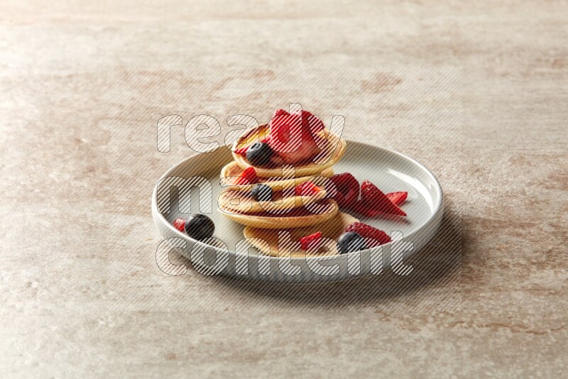 Five stacked mixed berries mini pancakes in a blue plate on beige background