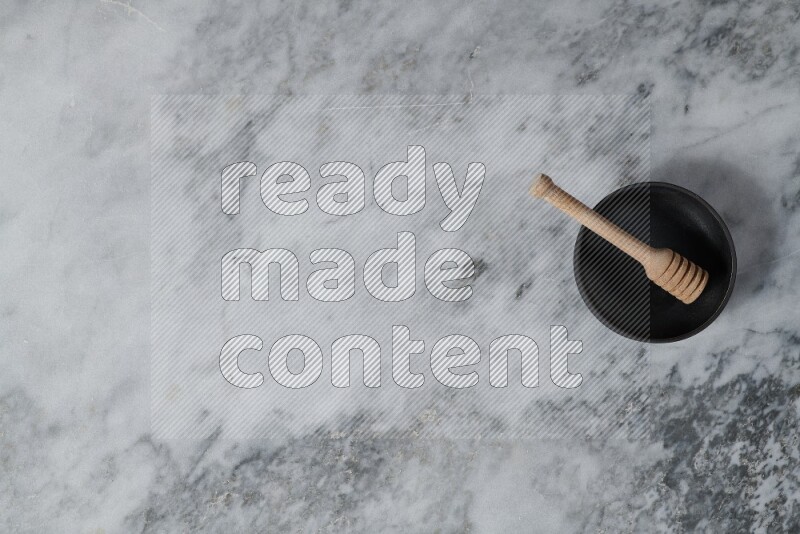 Black pottery bowl with wooden honey dipper in it on grey marble background