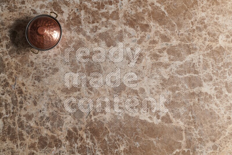A small copper pot on beige marble background