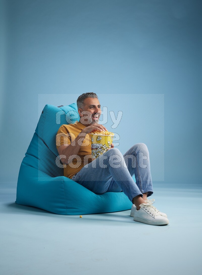 A man sitting on a blue beanbag and eating popcorn