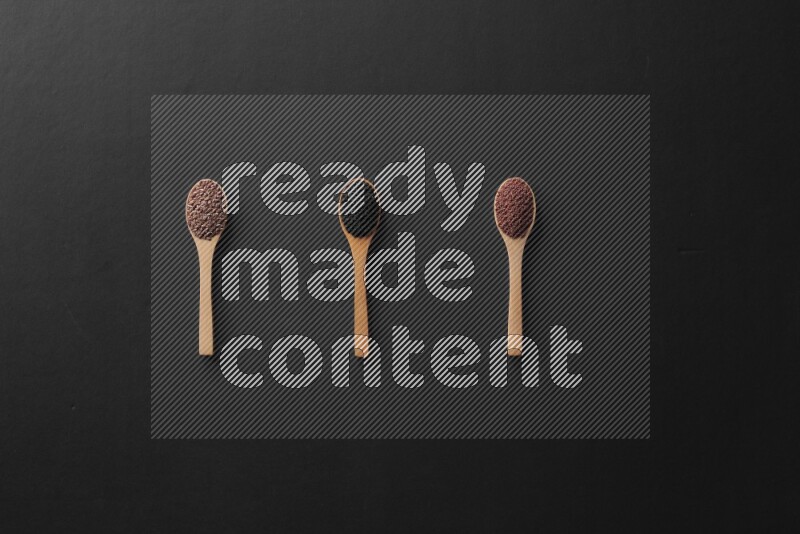wooden spoons filled with white peppers, mustard seeds, black seeds, garden cress, cumin and flax on black flooring