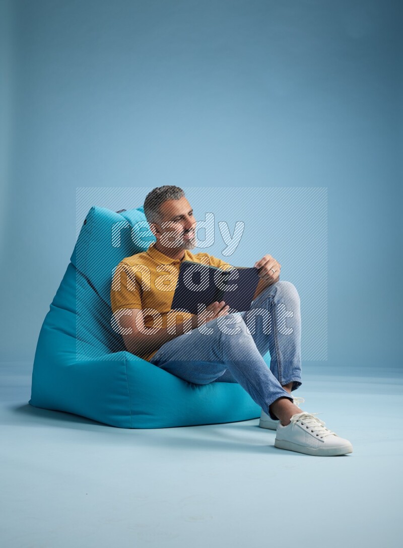 A man sitting on a blue beanbag and reading a book
