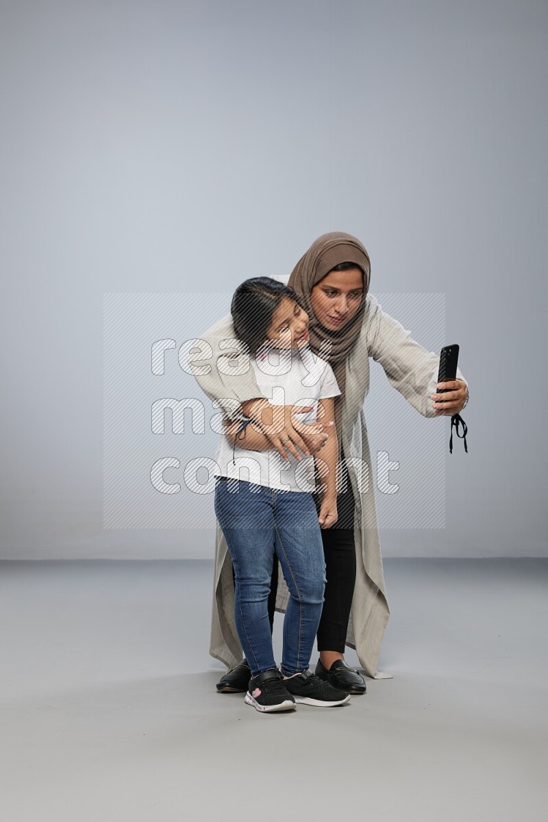 A girl standing taking selfie with her mother on gray background