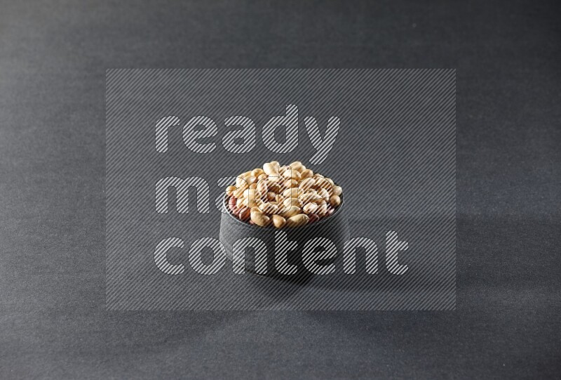 A black pottery bowl full of peeled peanuts on a black background in different angles