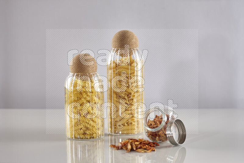 Raw pasta in glass jars with chilis on light grey background