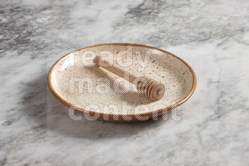 Beige pottery plate with wooden honey dipper in it on grey marble background