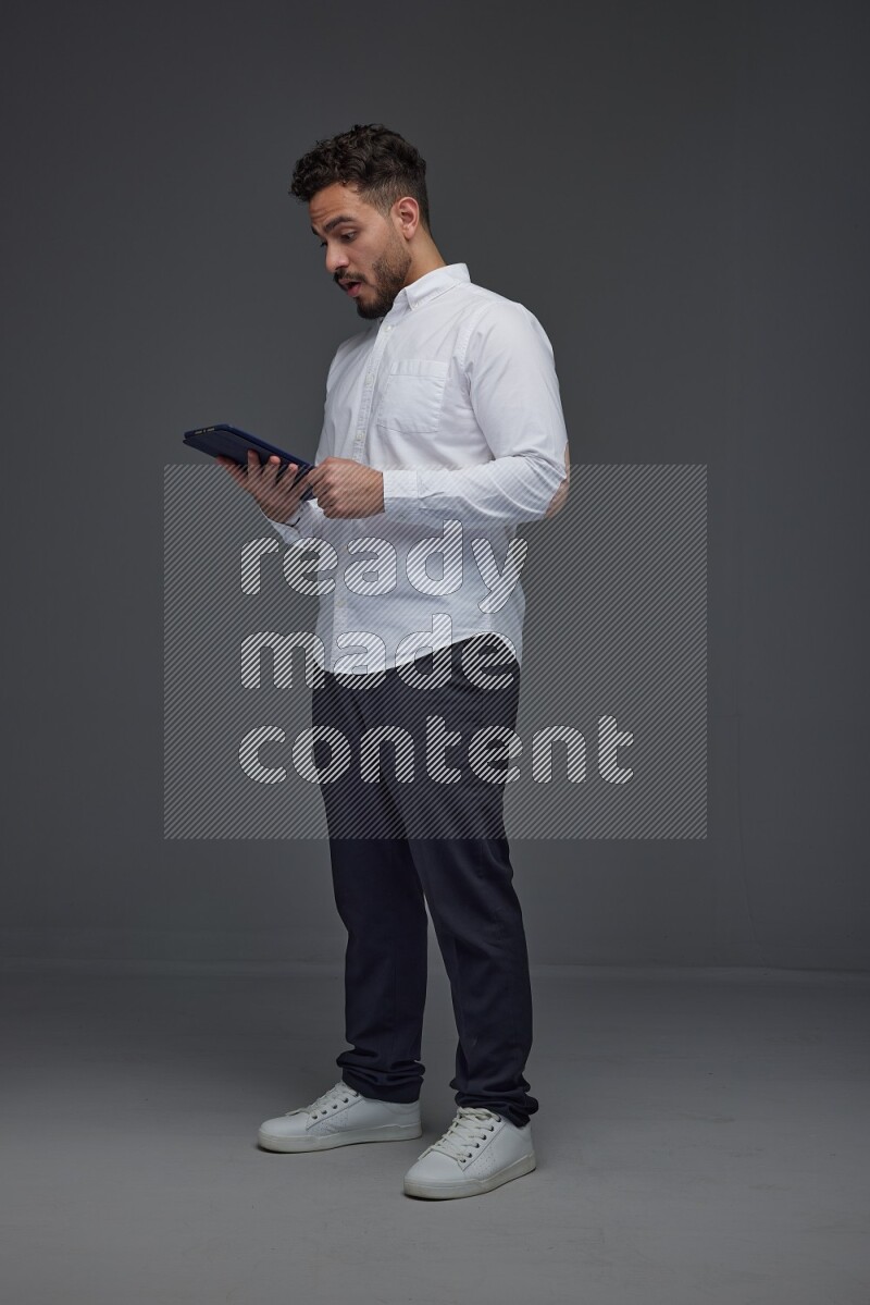 A man wearing smart casual standing and using his tablet eye level on a gray background