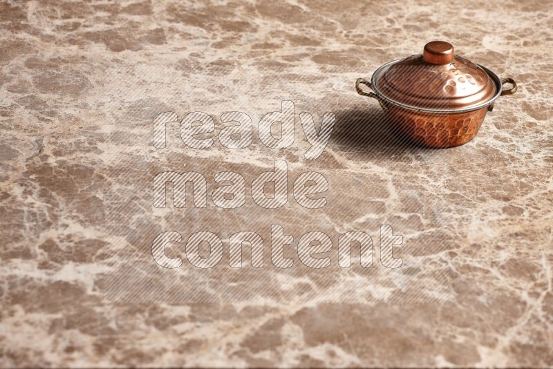 A small copper pot on beige marble background