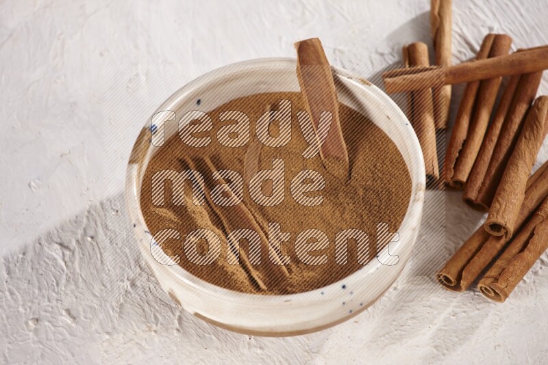 Ceramic bowl full of cinnamon powder with cinnamon sticks on the side on white background