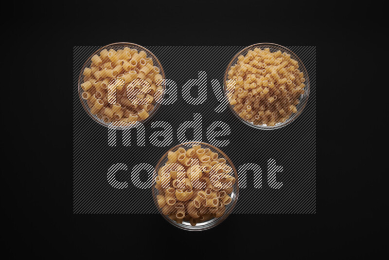 Different pasta types in glass bowls on black background