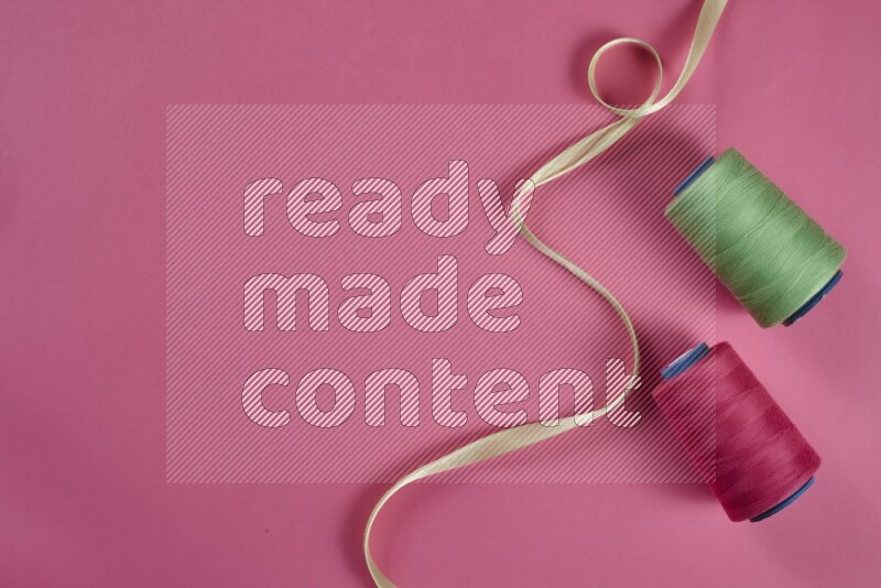 مجموعة من أدوات الخياطة والتفصيل خضراء وزهرية اللون على خلفية زهرية