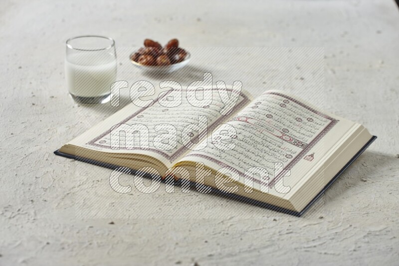 Quran with dates, prayer beads and different drinks all placed on textured white background