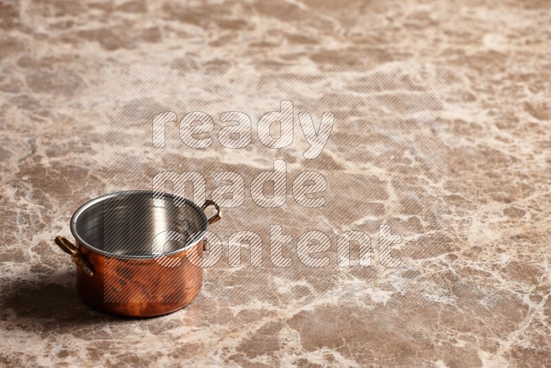 A small copper pot on beige marble background