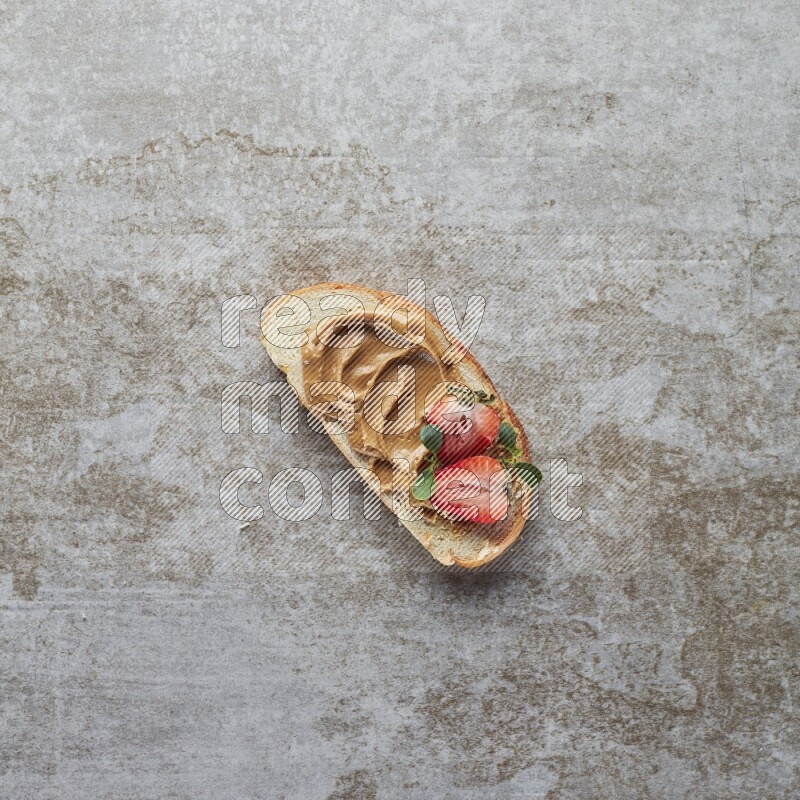 open faced peanut butter sandwich with strawberries on a grey textured background