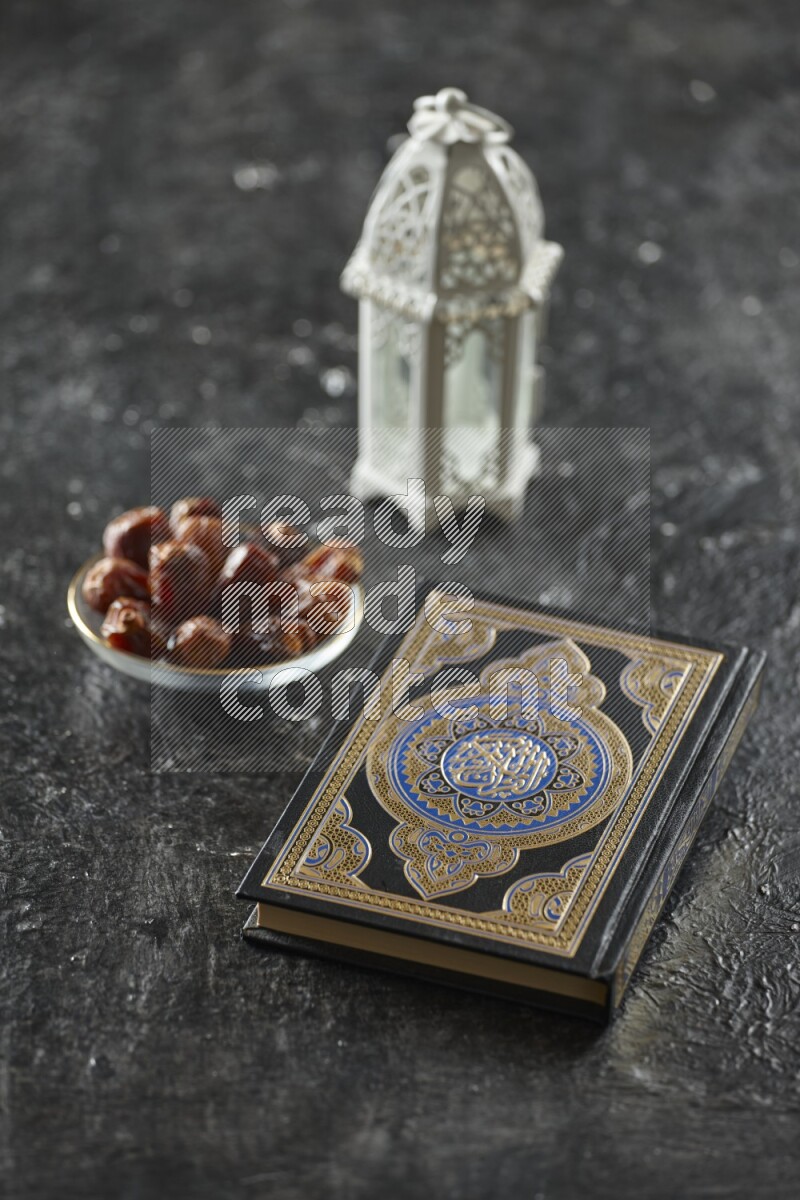 A white lantern with different drinks, dates, nuts, prayer beads and quran on textured black background