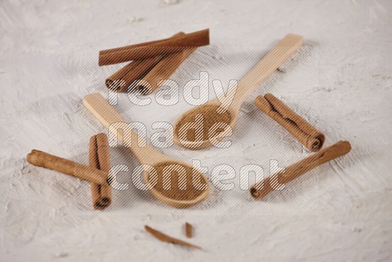 Two wooden spoons full of cinnamon powder with cinnamon sticks on white background