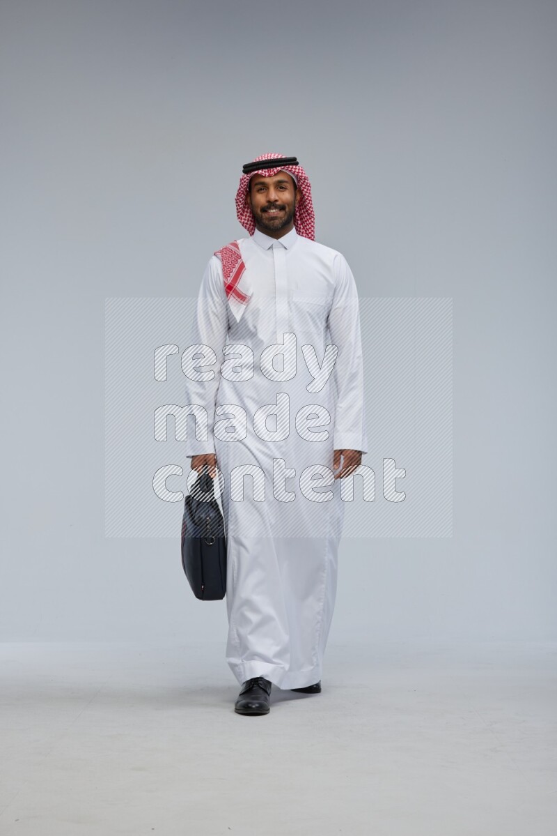 Saudi man Wearing Thob and shomag standing holding bag on Gray background