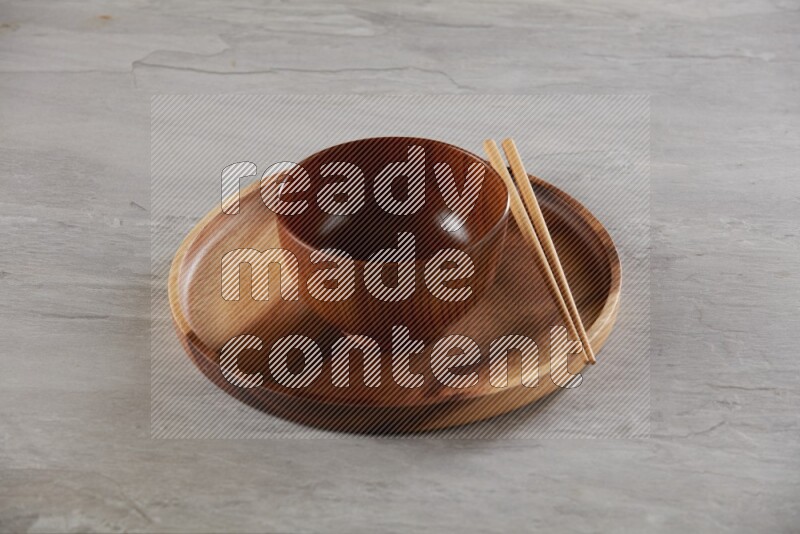 brown wood round bowl on top of brown wood round plate and wood chopsticks, on grey textured countertop
