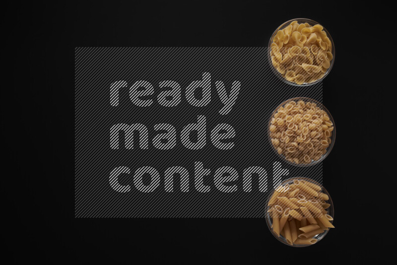 Different pasta types in 3 glass bowls on black background
