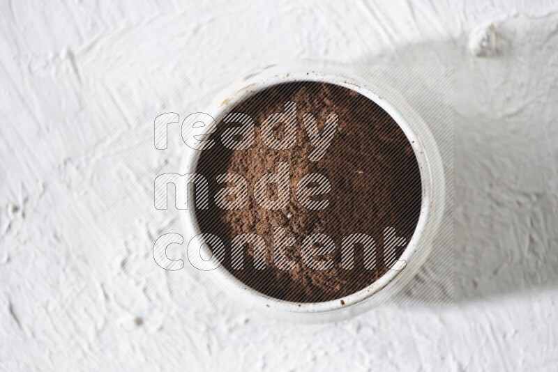 A beige ceramic bowl full of cloves powder on a white flooring