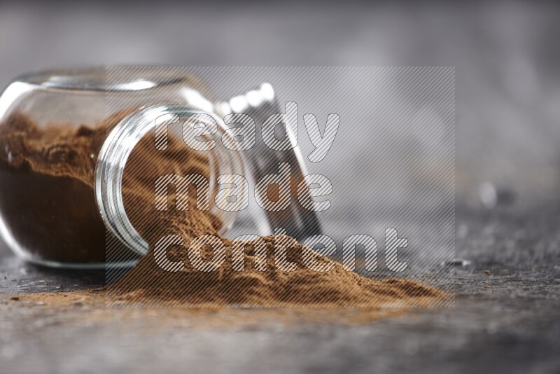 Flipped herbal glass jar full of cinnamon powder on textured black background