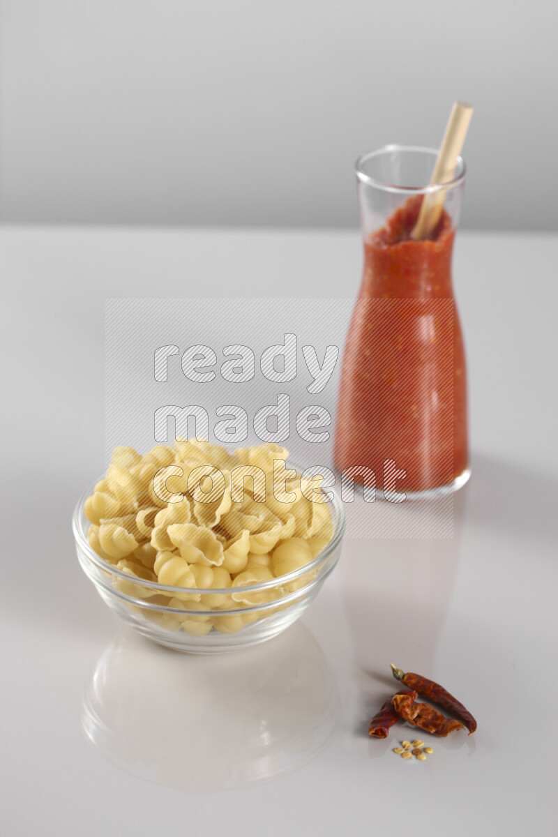 Raw pasta with tomatoe pasta with different ingredients such as cherry tomatoes, basil, garlic, bay laurel, cardamom, white pepper, black pepper, red chilis and wheat stalks on light grey background
