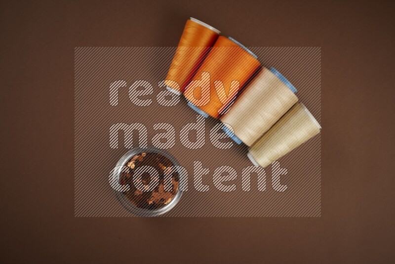 An orange collection of sewing and tailoring tools arranged on a brown background