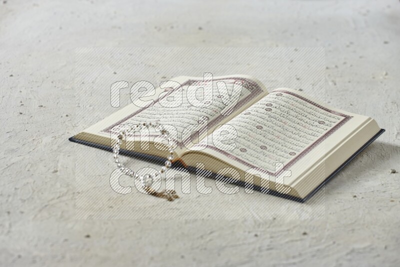 Quran with dates, prayer beads and different drinks all placed on textured white background