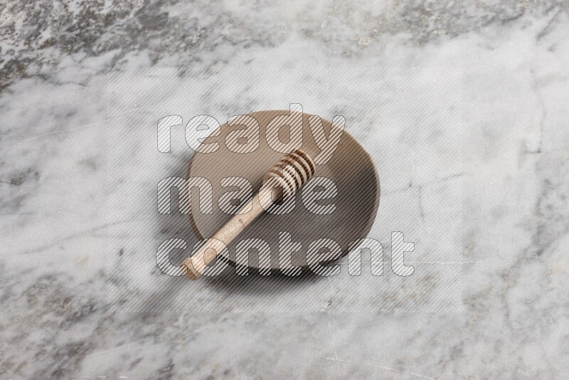 Multicolored pottery plate with wooden honey dipper in it on grey marble background