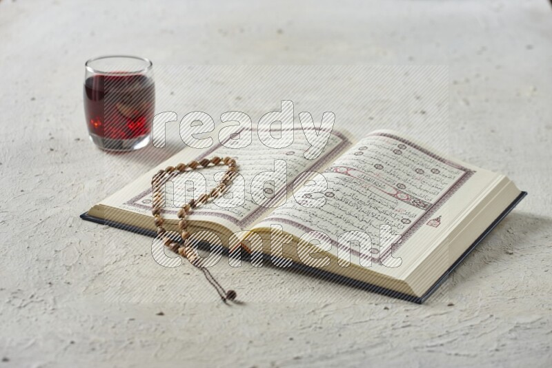 Quran with dates, prayer beads and different drinks all placed on textured white background