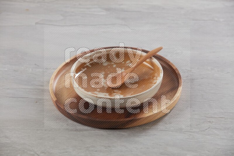 multi color pottery round dish on top of brown wood round plate and spoon, on grey textured countertop