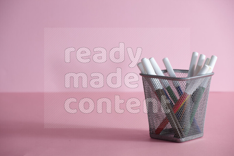 Pens, pencils and other different school supplies in a metal pen holder on rose background