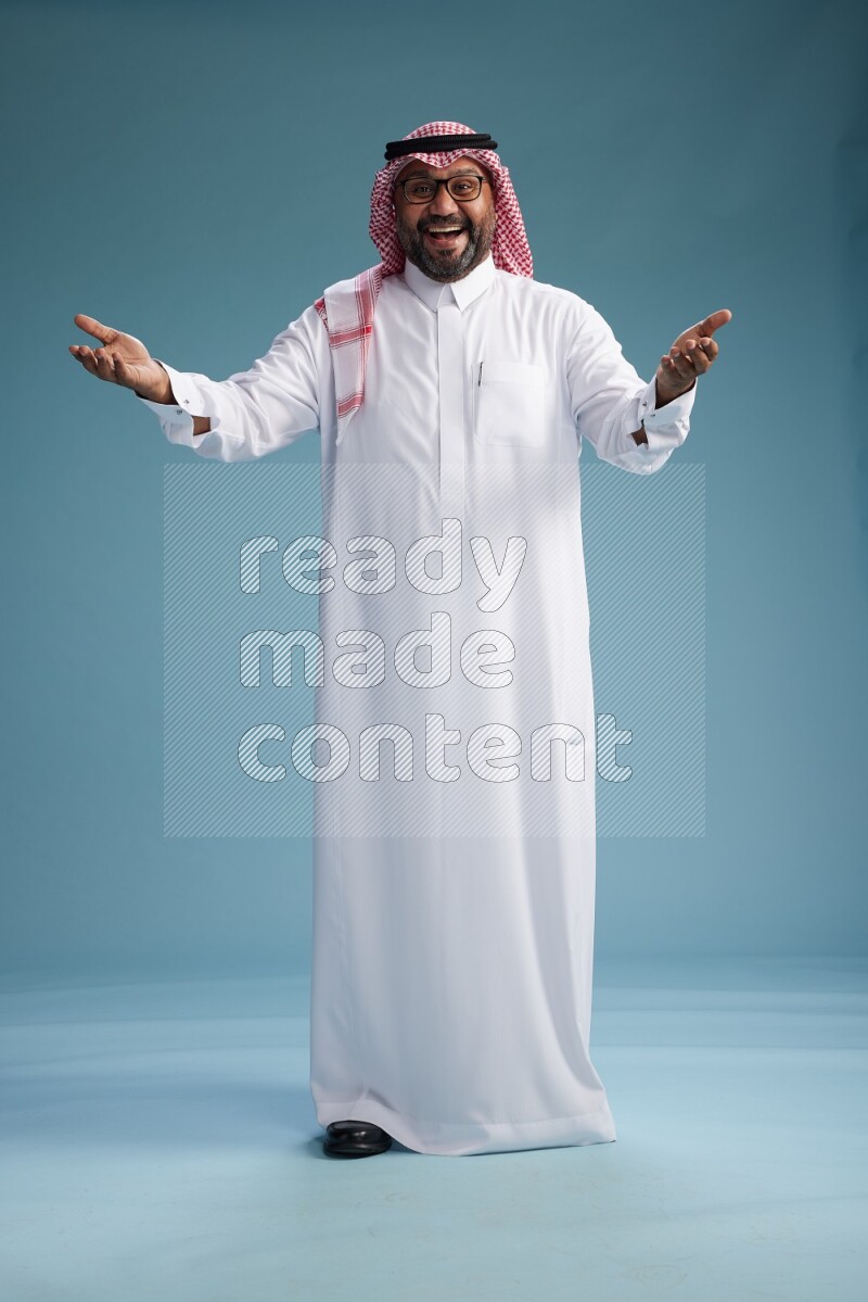 Saudi Man with shimag Standing Interacting with the camera on blue background