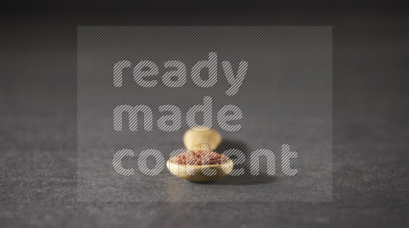 A wooden spoon full of garden cress seeds on a black flooring