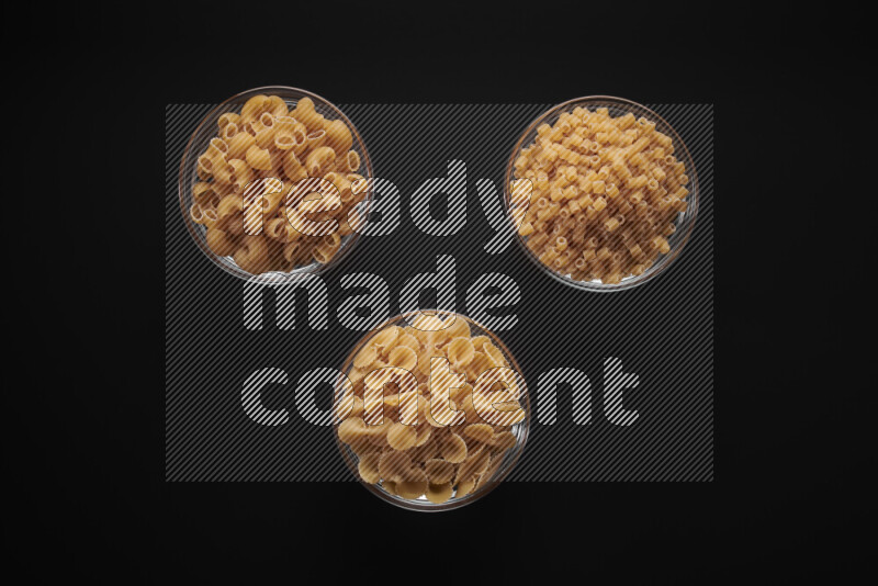 Different pasta types in glass bowls on black background