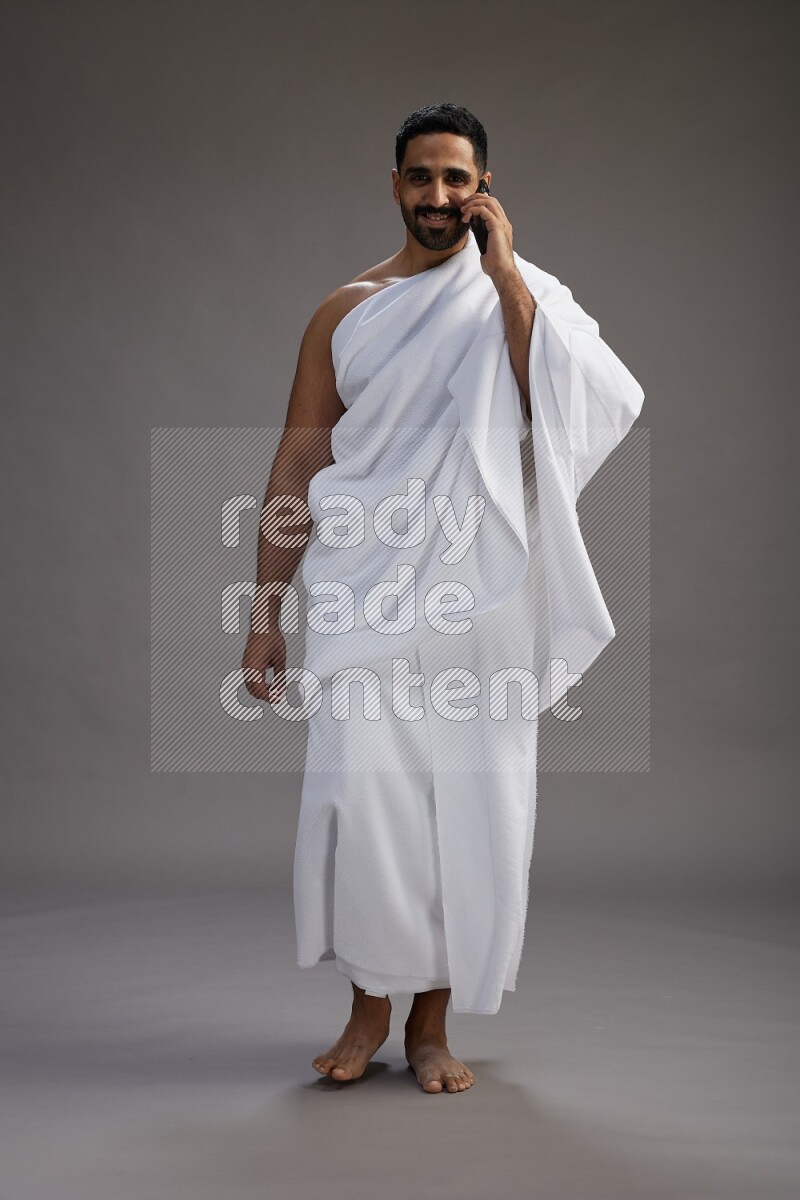 A man wearing Ehram Standing talking on phone on gray background