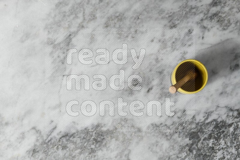 Multicolored pottery cup with wooden honey dipper in it on grey marble background