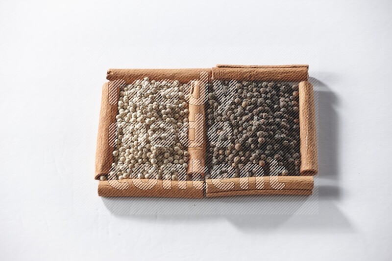 2 squares of cinnamon sticks full of black pepper and white pepper on white flooring
