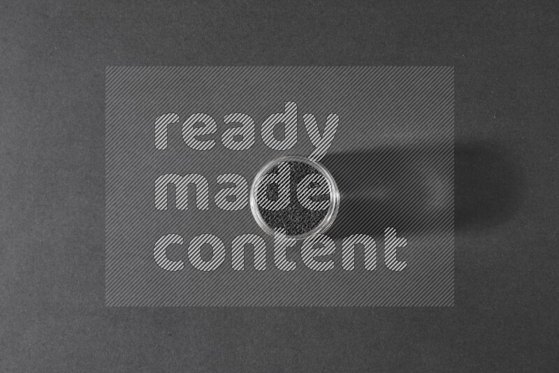 A glass jar full of black seeds on a black flooring