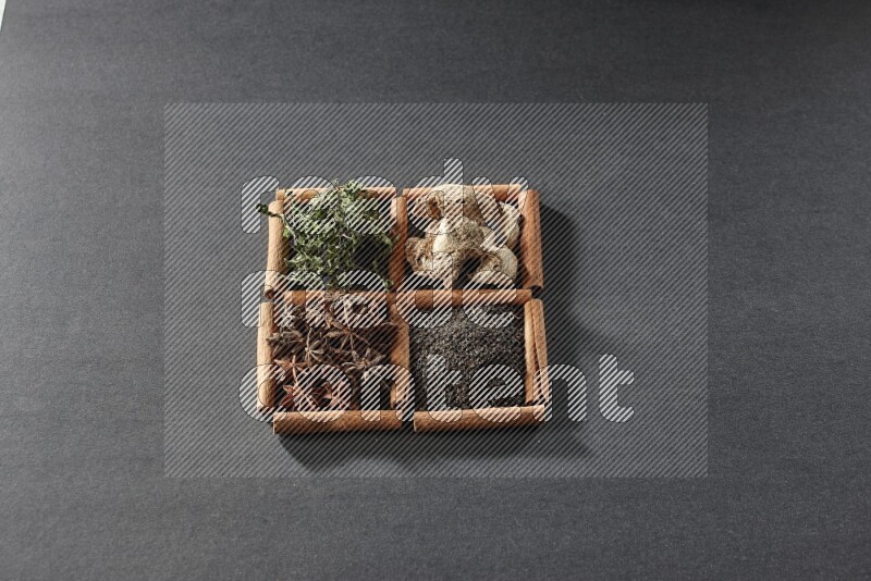 4 squares of cinnamon sticks full of black tea, dried ginger, dried mint leaves and star anise on black flooring