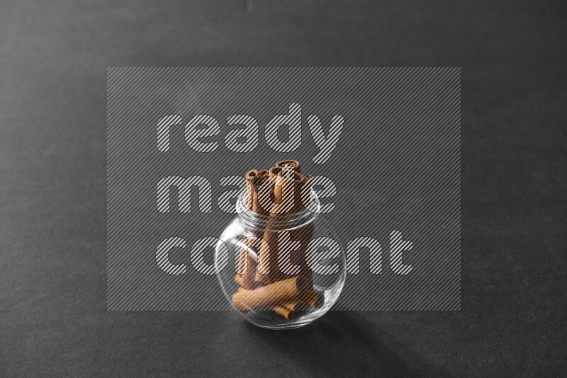 A glass spice jar full of cinnamon sticks on black flooring