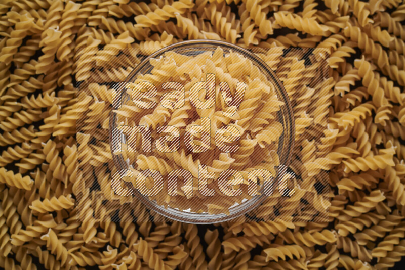 Fusilli pasta in a glass bowl on black background