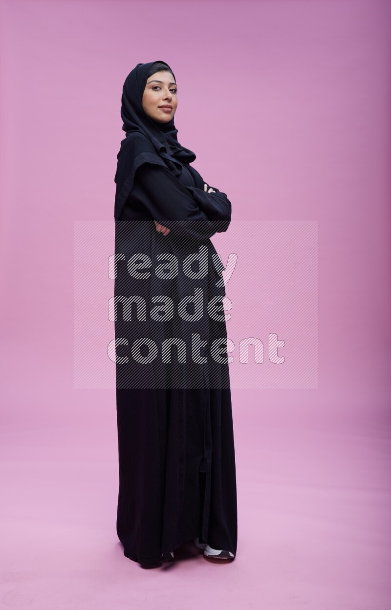 Saudi woman wearing Abaya standing with crossed arms on pink background