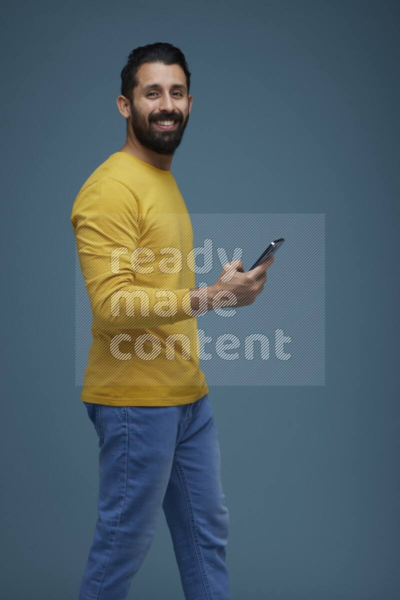 Man posing with a phone in a blue background wearing a yellow shirt