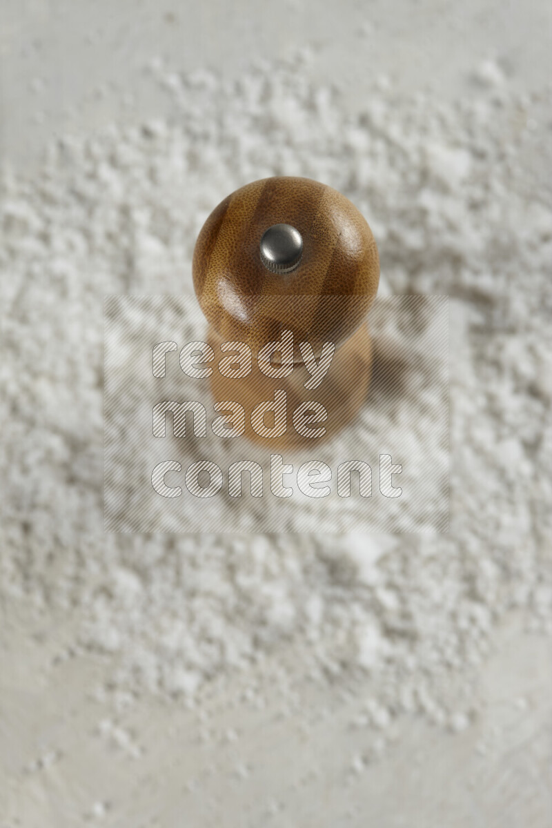 A wooden grinder standing upright and surrounded by coarse white seaa salt on white background