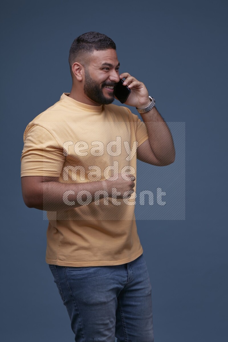 رجل يرتدي بنطال ازرق جينز وقميص اصفر بأكمام قصيره يتحدث بجواله