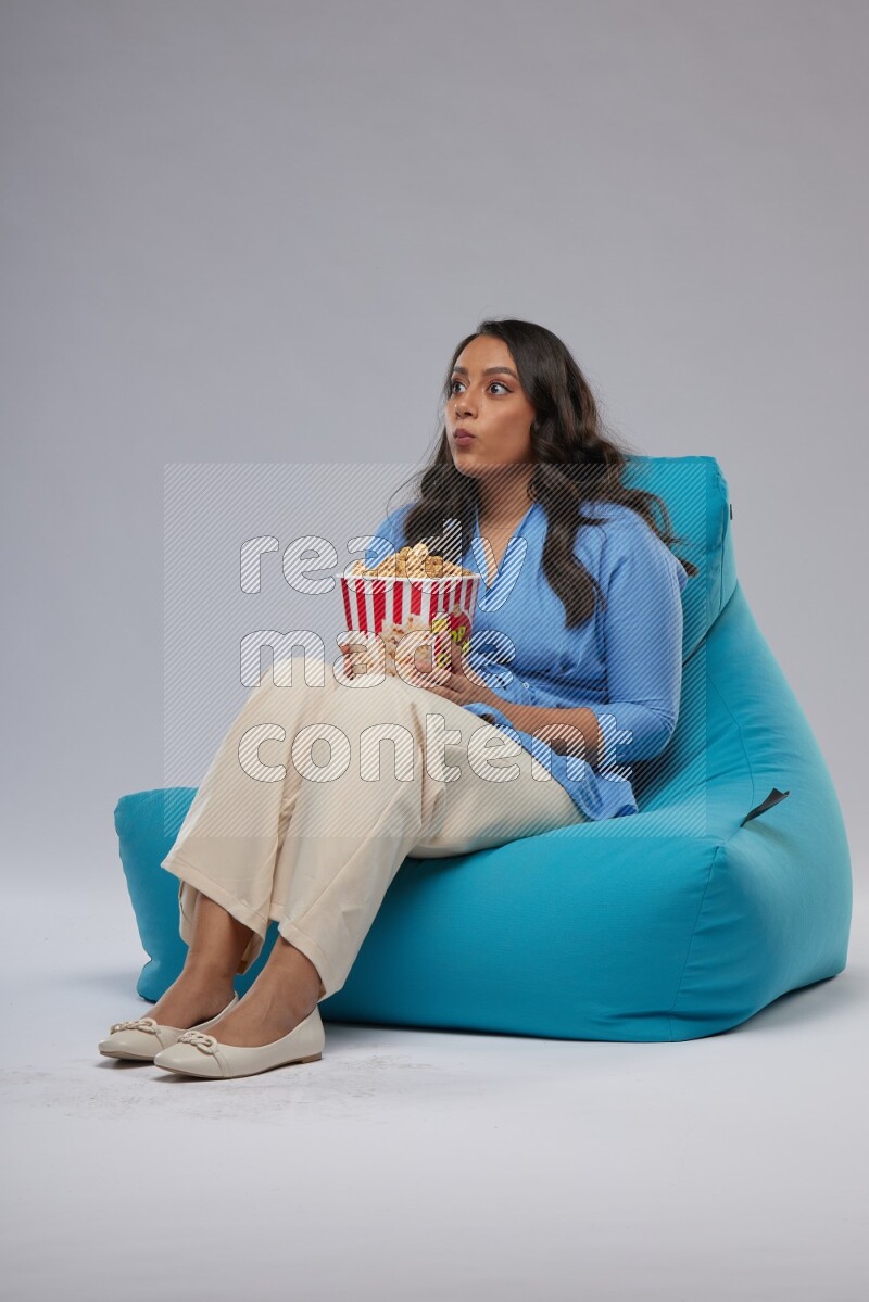 A woman sitting on a blue beanbag and eating popcorn