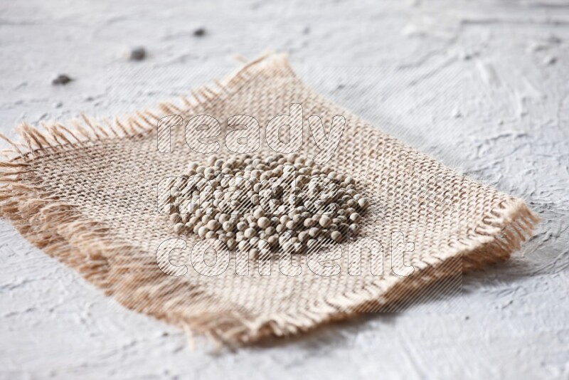 White pepper beads on a burlap piece of fabric on textured white flooring